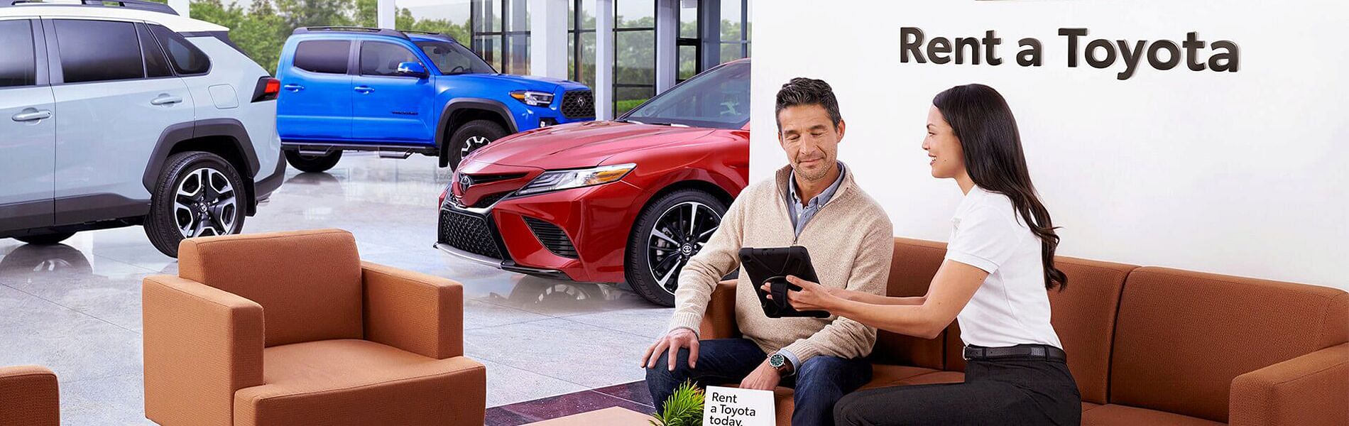 Woman shows man cars for rent sitting in car showroom