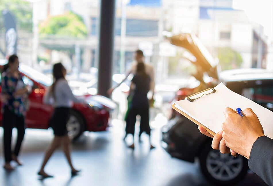 Person holding a checklist with people inside a dealership in the background